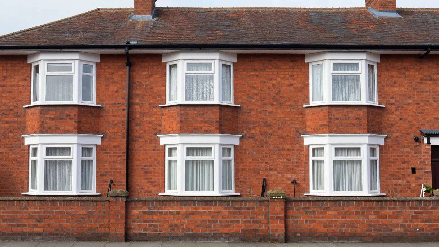 A row of red brick semi-detached houses with white bay windows behind a low brick garden wall