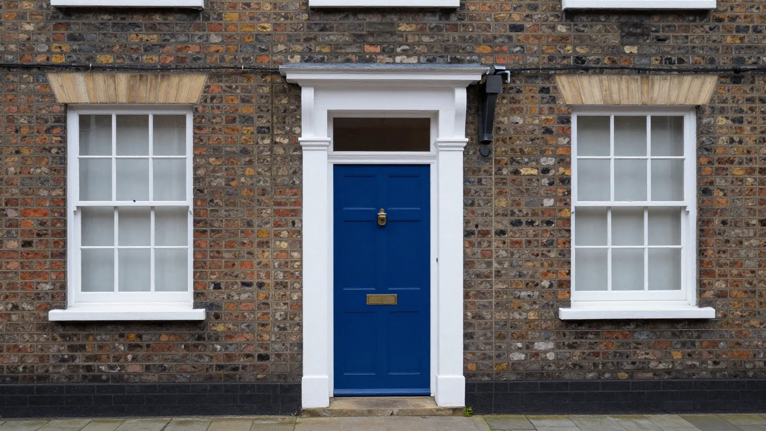 A blue panelled front door with a brass knocker and letter plate in a flint and brick house front