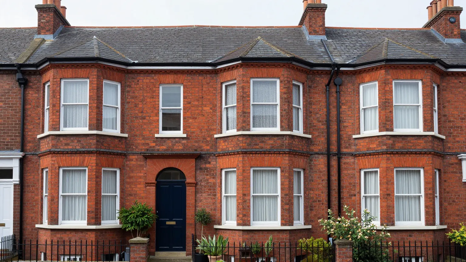 A terrace of red brick Victorian houses with bay windows, slate roofs and small front gardens on an overcast day